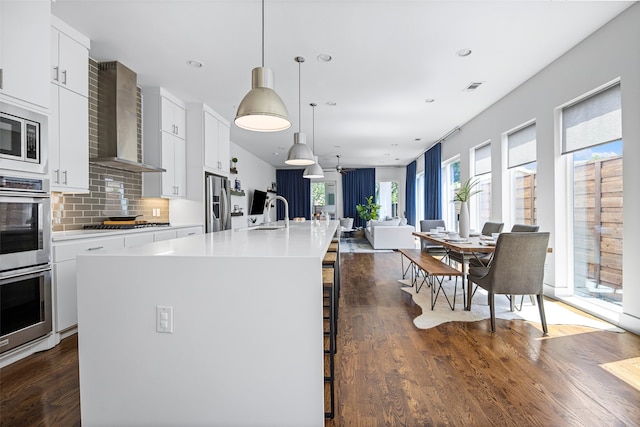 kitchen featuring wall chimney exhaust hood, a breakfast bar area, a center island with sink, and white cabinets