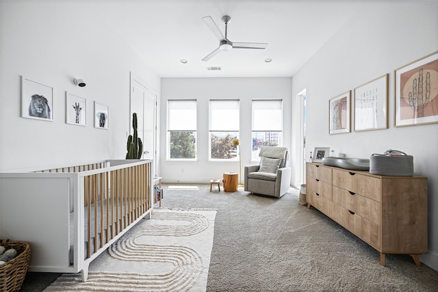 carpeted bedroom with ceiling fan and a nursery area