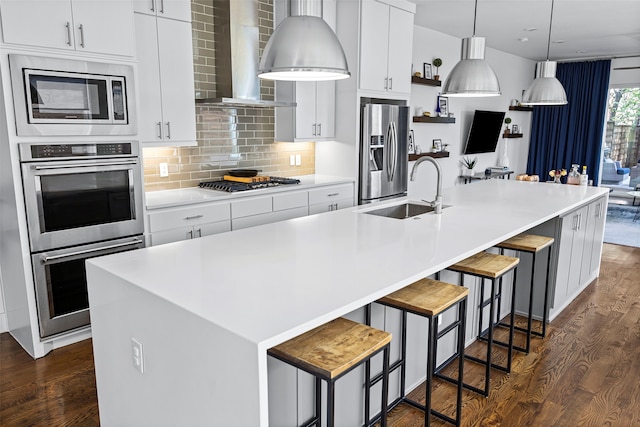 kitchen featuring wall chimney exhaust hood, appliances with stainless steel finishes, an island with sink, and a kitchen breakfast bar