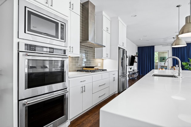 kitchen with sink, stainless steel appliances, wall chimney exhaust hood, pendant lighting, and white cabinets