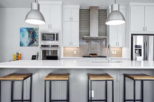 kitchen with decorative backsplash, wall chimney exhaust hood, a kitchen breakfast bar, hanging light fixtures, and stainless steel appliances