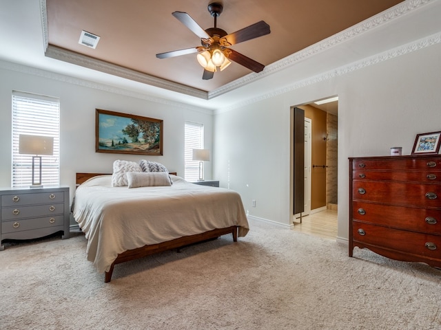 bedroom featuring light carpet, a tray ceiling, crown molding, ensuite bathroom, and ceiling fan