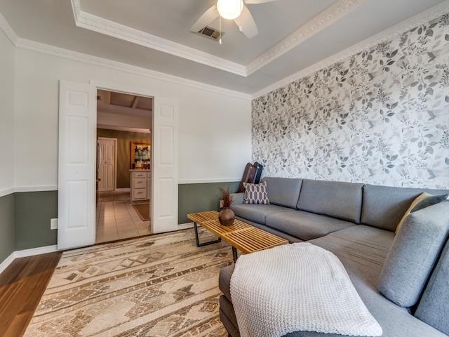 living room with crown molding, wood-type flooring, a tray ceiling, and ceiling fan