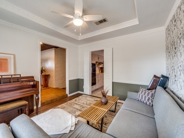 living room with crown molding, hardwood / wood-style flooring, a tray ceiling, and ceiling fan