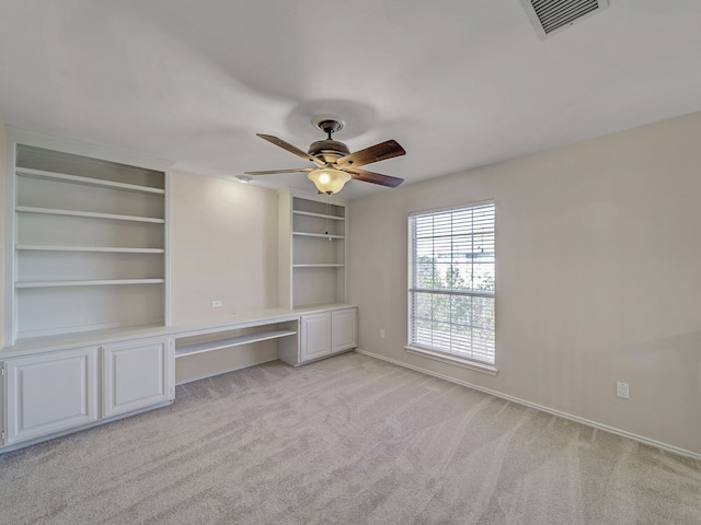 unfurnished living room featuring light carpet, built in desk, built in features, and ceiling fan