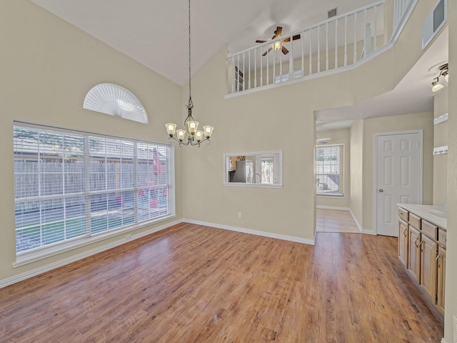 unfurnished dining area with ceiling fan with notable chandelier, high vaulted ceiling, and light wood-type flooring