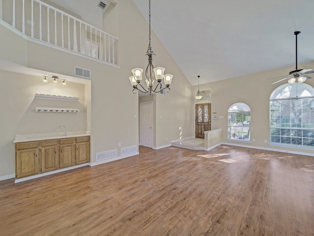 unfurnished living room featuring ceiling fan with notable chandelier, high vaulted ceiling, and light hardwood / wood-style floors