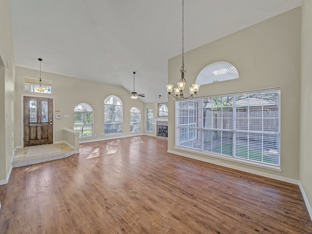 unfurnished dining area with hardwood / wood-style flooring, ceiling fan with notable chandelier, and high vaulted ceiling