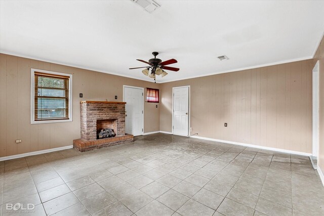 unfurnished living room featuring a brick fireplace, crown molding, light tile patterned floors, and ceiling fan