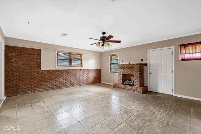 unfurnished living room with ceiling fan, crown molding, brick wall, and a brick fireplace