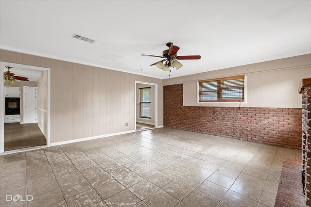 unfurnished room featuring tile patterned flooring, ceiling fan, ornamental molding, and brick wall