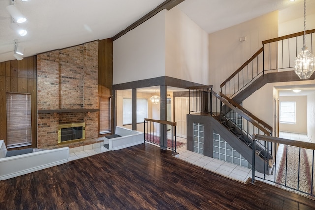 unfurnished living room featuring hardwood / wood-style flooring, a chandelier, a fireplace, high vaulted ceiling, and wood walls