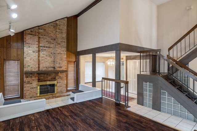 unfurnished living room with light hardwood / wood-style flooring, a notable chandelier, a fireplace, high vaulted ceiling, and wood walls