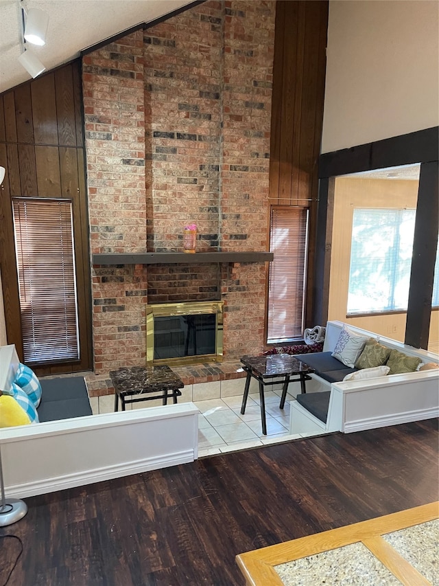 living room featuring wood-type flooring, brick wall, a fireplace, high vaulted ceiling, and wood walls