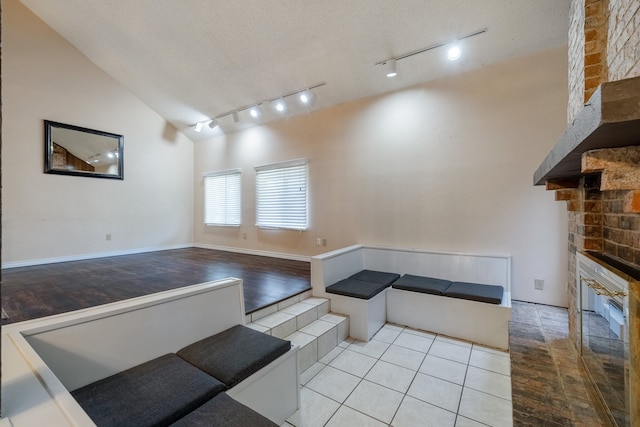 living room with light hardwood / wood-style floors, a stone fireplace, track lighting, and vaulted ceiling