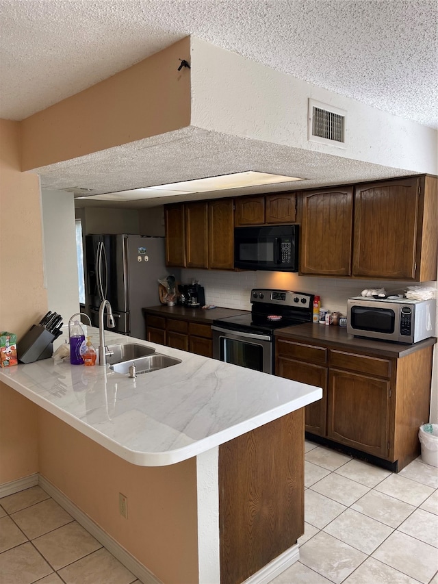 kitchen featuring sink, a textured ceiling, kitchen peninsula, stainless steel appliances, and light tile patterned floors