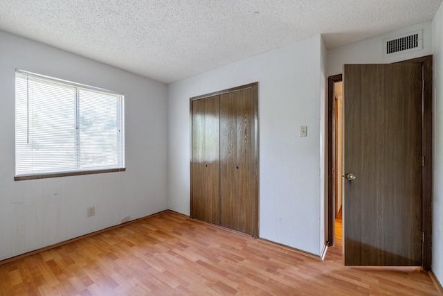 unfurnished bedroom featuring a closet, a textured ceiling, and light wood-type flooring