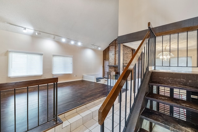 staircase featuring a notable chandelier, track lighting, high vaulted ceiling, and wood-type flooring