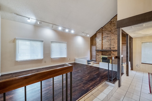 unfurnished living room with a brick fireplace, a textured ceiling, high vaulted ceiling, and light tile patterned floors