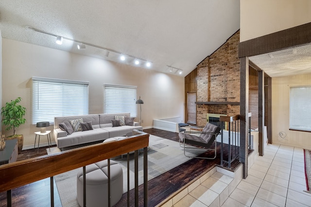 tiled living room featuring a textured ceiling, rail lighting, high vaulted ceiling, and a brick fireplace