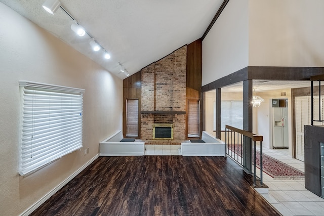 unfurnished living room with a textured ceiling, a fireplace, light wood-type flooring, and high vaulted ceiling