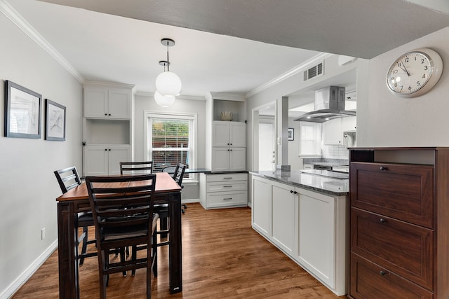 kitchen with hardwood / wood-style floors, exhaust hood, hanging light fixtures, ornamental molding, and white cabinetry