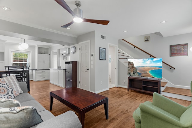 living room with light wood-type flooring, ceiling fan, and ornamental molding