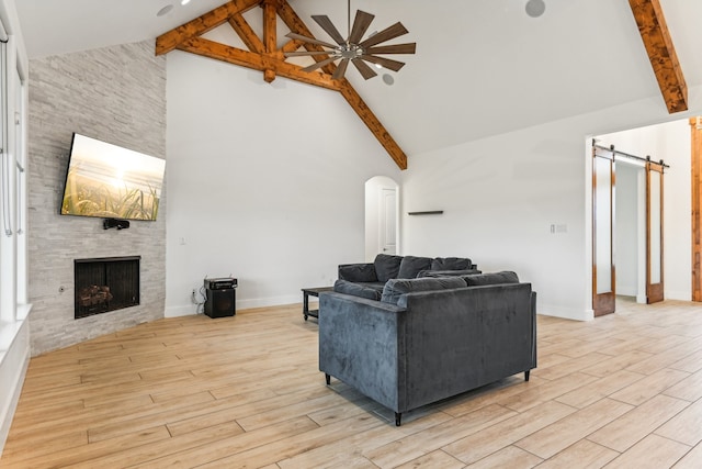 living room with a barn door, light wood-type flooring, a fireplace, high vaulted ceiling, and ceiling fan