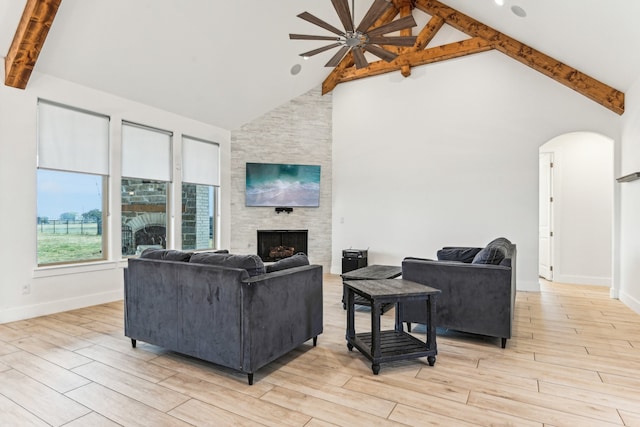 living room featuring beamed ceiling, light hardwood / wood-style floors, a stone fireplace, and high vaulted ceiling