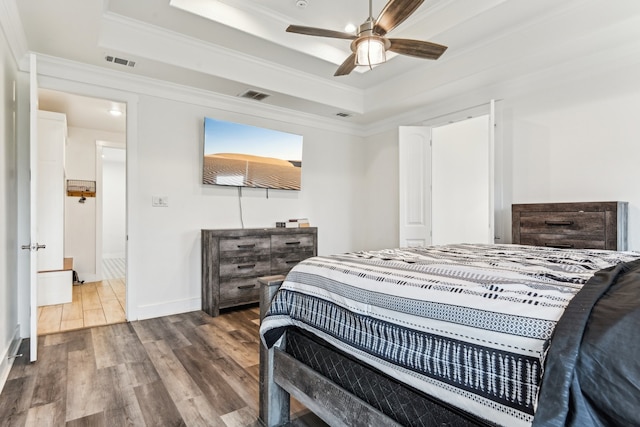 bedroom with ornamental molding, hardwood / wood-style flooring, a tray ceiling, and ceiling fan