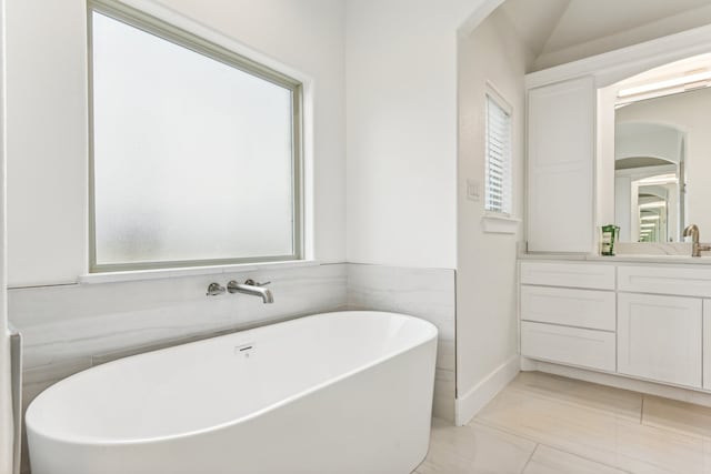 bathroom featuring vanity, a tub to relax in, a healthy amount of sunlight, and tile walls