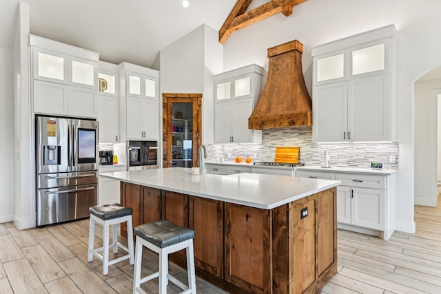 kitchen featuring custom range hood, white cabinets, appliances with stainless steel finishes, and a kitchen island with sink