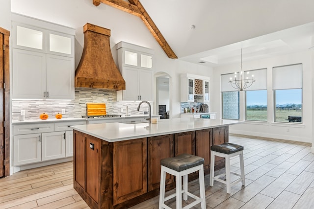 kitchen with custom exhaust hood, white cabinetry, a kitchen island with sink, and vaulted ceiling with beams