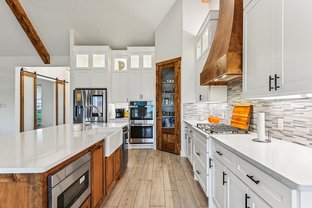 kitchen with light stone countertops, a barn door, stainless steel appliances, white cabinets, and premium range hood