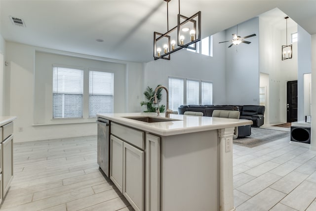 kitchen with decorative light fixtures, stainless steel dishwasher, sink, and a kitchen island with sink