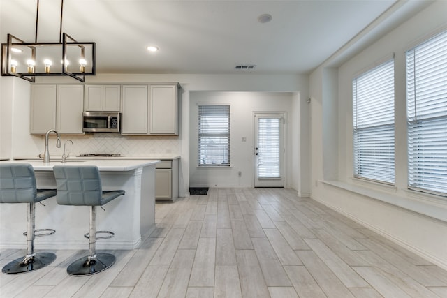 kitchen with light hardwood / wood-style floors, a chandelier, a breakfast bar area, gray cabinetry, and pendant lighting