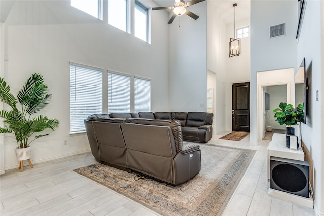 living room featuring a high ceiling, ceiling fan with notable chandelier, and light wood-type flooring