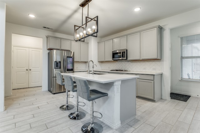 kitchen with gray cabinets, pendant lighting, a kitchen island with sink, and stainless steel appliances