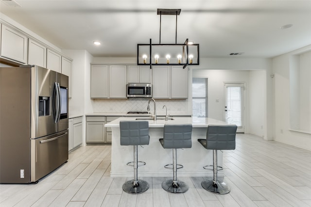 kitchen featuring stainless steel appliances, decorative light fixtures, decorative backsplash, sink, and a kitchen island with sink