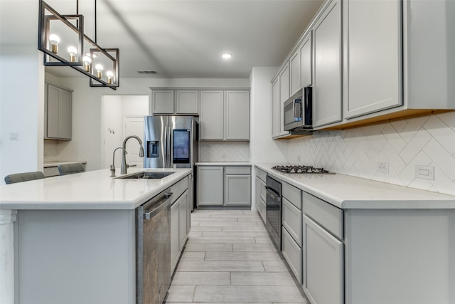 kitchen with stainless steel appliances, hanging light fixtures, sink, an island with sink, and gray cabinetry