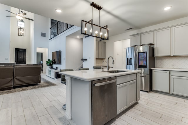 kitchen featuring a center island with sink, sink, gray cabinetry, appliances with stainless steel finishes, and decorative light fixtures