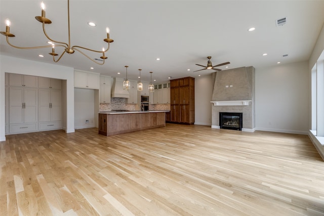 unfurnished living room featuring a fireplace, ceiling fan with notable chandelier, and light hardwood / wood-style flooring