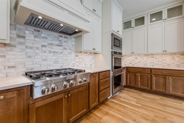 kitchen with light hardwood / wood-style floors, sink, a kitchen island with sink, pendant lighting, and premium range hood