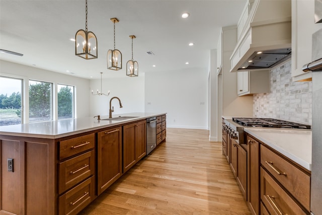 kitchen with hanging light fixtures, ceiling fan with notable chandelier, a center island with sink, and light hardwood / wood-style flooring