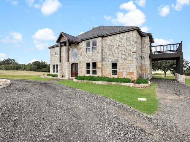 exterior space with a deck, a shingled roof, stone siding, a front lawn, and dirt driveway