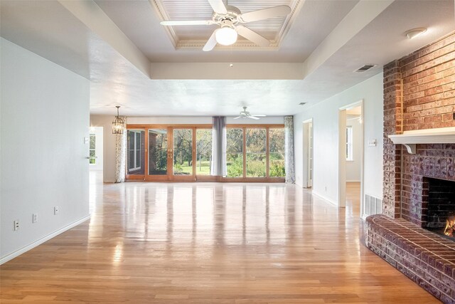 unfurnished living room with a raised ceiling, a fireplace, ceiling fan with notable chandelier, and light wood-type flooring