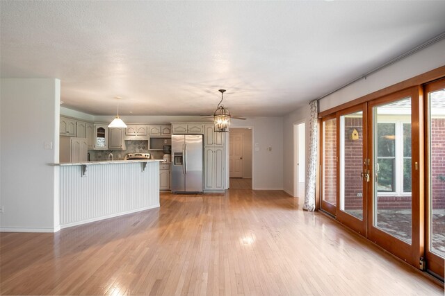 kitchen with french doors, light hardwood / wood-style flooring, appliances with stainless steel finishes, a notable chandelier, and kitchen peninsula