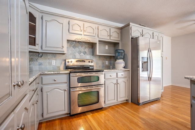 kitchen featuring light stone counters, backsplash, light hardwood / wood-style floors, a textured ceiling, and appliances with stainless steel finishes