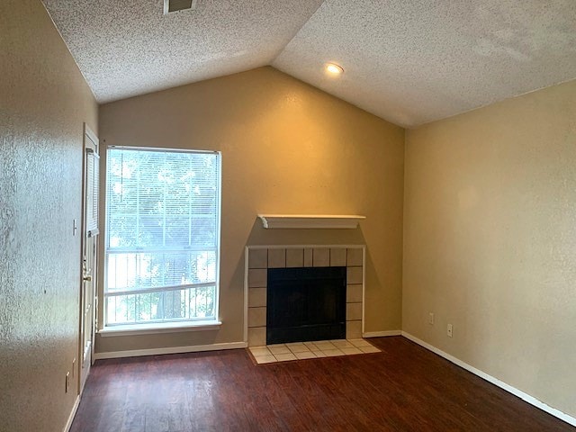 unfurnished living room featuring wood-type flooring, vaulted ceiling, a tile fireplace, and a textured ceiling