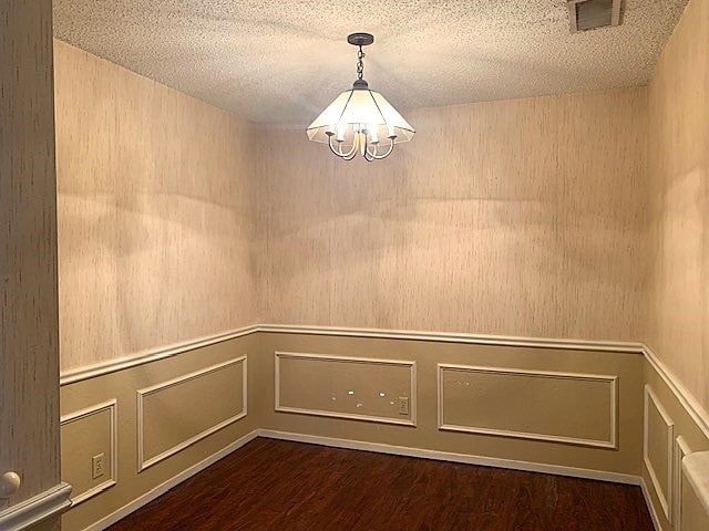 unfurnished room with dark hardwood / wood-style floors, a textured ceiling, and a notable chandelier